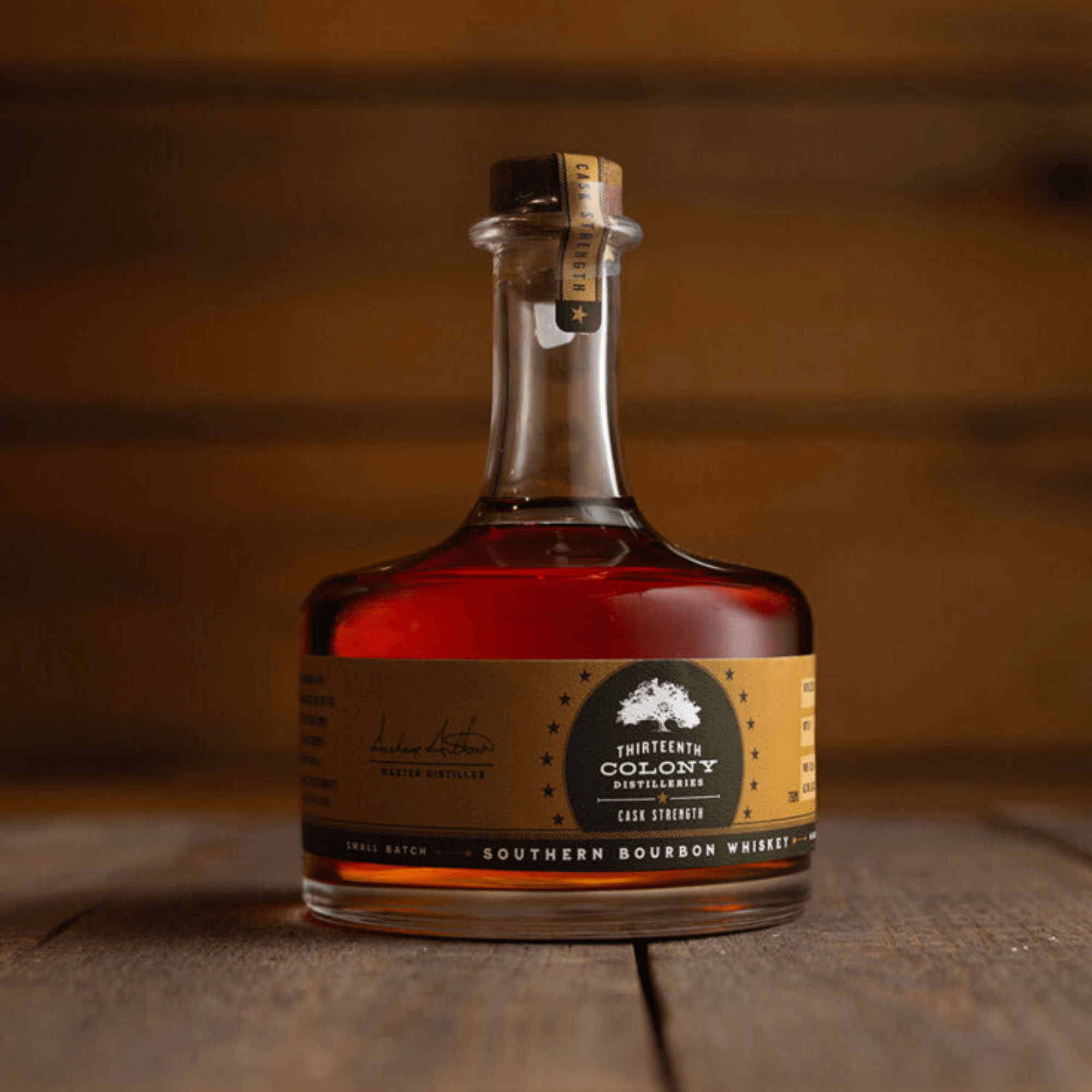 Thirteenth Colony Cask Strength Bourbon 750ml bottle on a wooden surface, showcasing its rich amber color and elegant label.